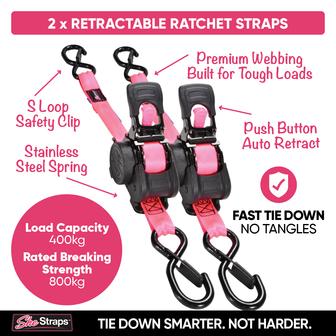 Two pink and black retractable ratchet straps shown on a white background with pink callout labels and text highlighting features like S-loop safety clip, stainless steel spring, push button auto retract, and load capacity 400kg / rated breaking strength 800kg. A SheStraps logo appears at the bottom.
